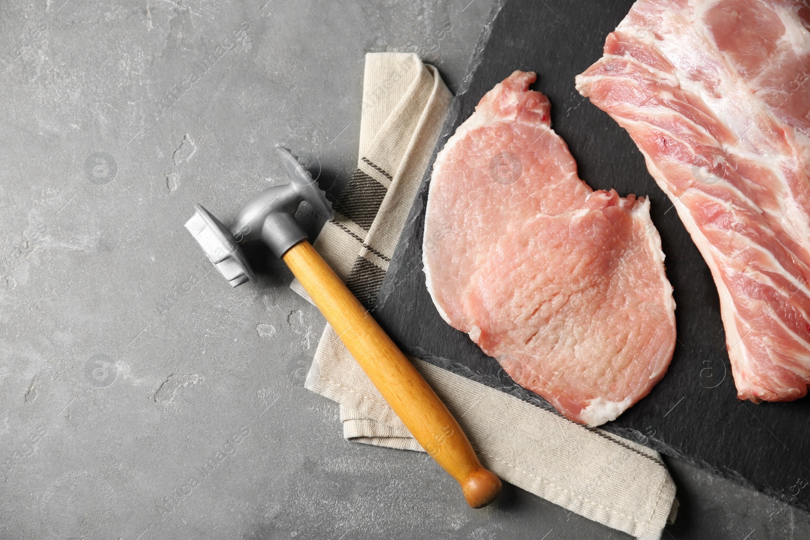 Photo of Cooking schnitzel. Raw pork chops with meat mallet on grey table, flat lay and space for text