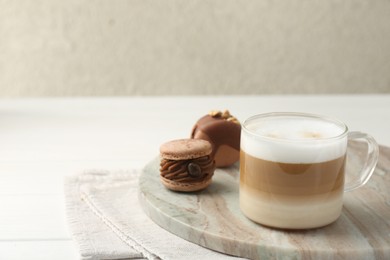 Aromatic coffee in cup and tasty macarons on white wooden table, space for text