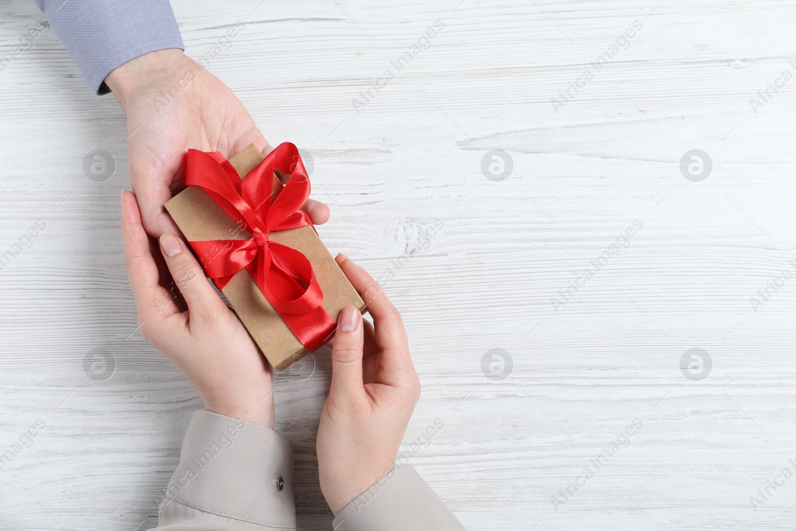 Photo of Man giving gift box to woman on white wooden table, top view. Space for text