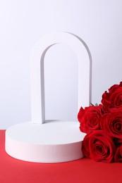 Photo of Stylish presentation for product. Geometric figures and roses on red table against white background