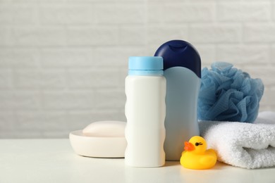 Baby cosmetic products, bath duck, sponge and towel on white table against brick wall. Space for text