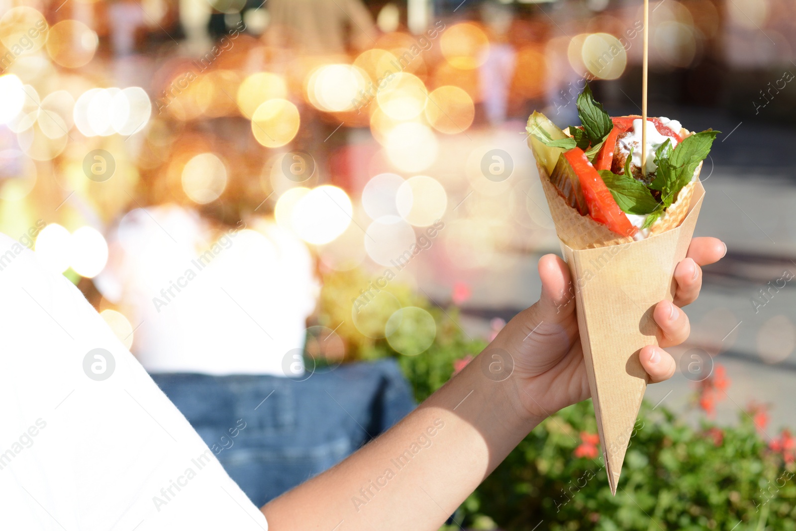 Photo of Woman holding wafer with falafel and vegetables outdoors, closeup. Street food