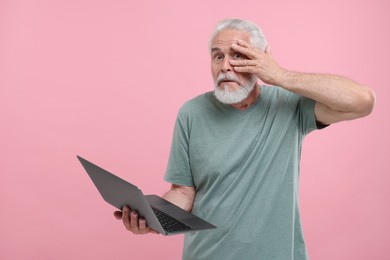 Photo of Embarrassed senior man holding laptop on pink background. Space for text