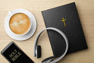 Bible, phone, cup of coffee and headphones on wooden background, flat lay. Religious audiobook