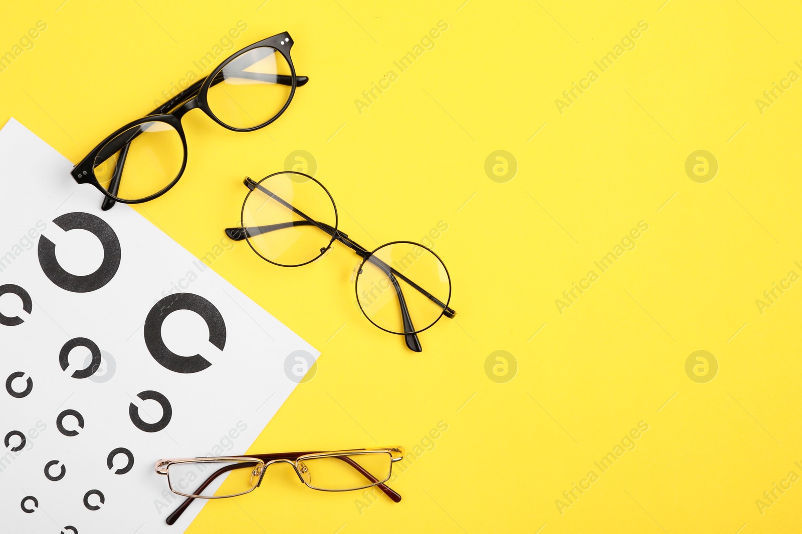 Photo of Vision test chart and glasses on yellow background, flat lay. Space for text