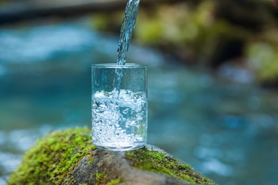 Photo of Fresh water pouring into glass on stone with moss near river. Space for text