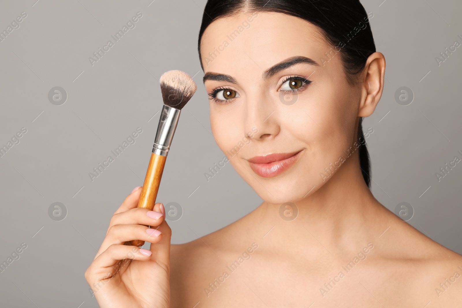 Photo of Beautiful young woman applying face powder with brush on grey background, closeup