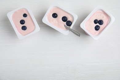 Photo of Plastic cups with tasty yogurts and blueberries on white wooden table, flat lay. Space for text