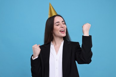 Happy woman in party hat on light blue background