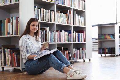 Photo of Young woman with book on floor in library