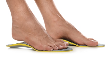 Photo of Man fitting orthopedic insoles on white background, closeup. Foot care
