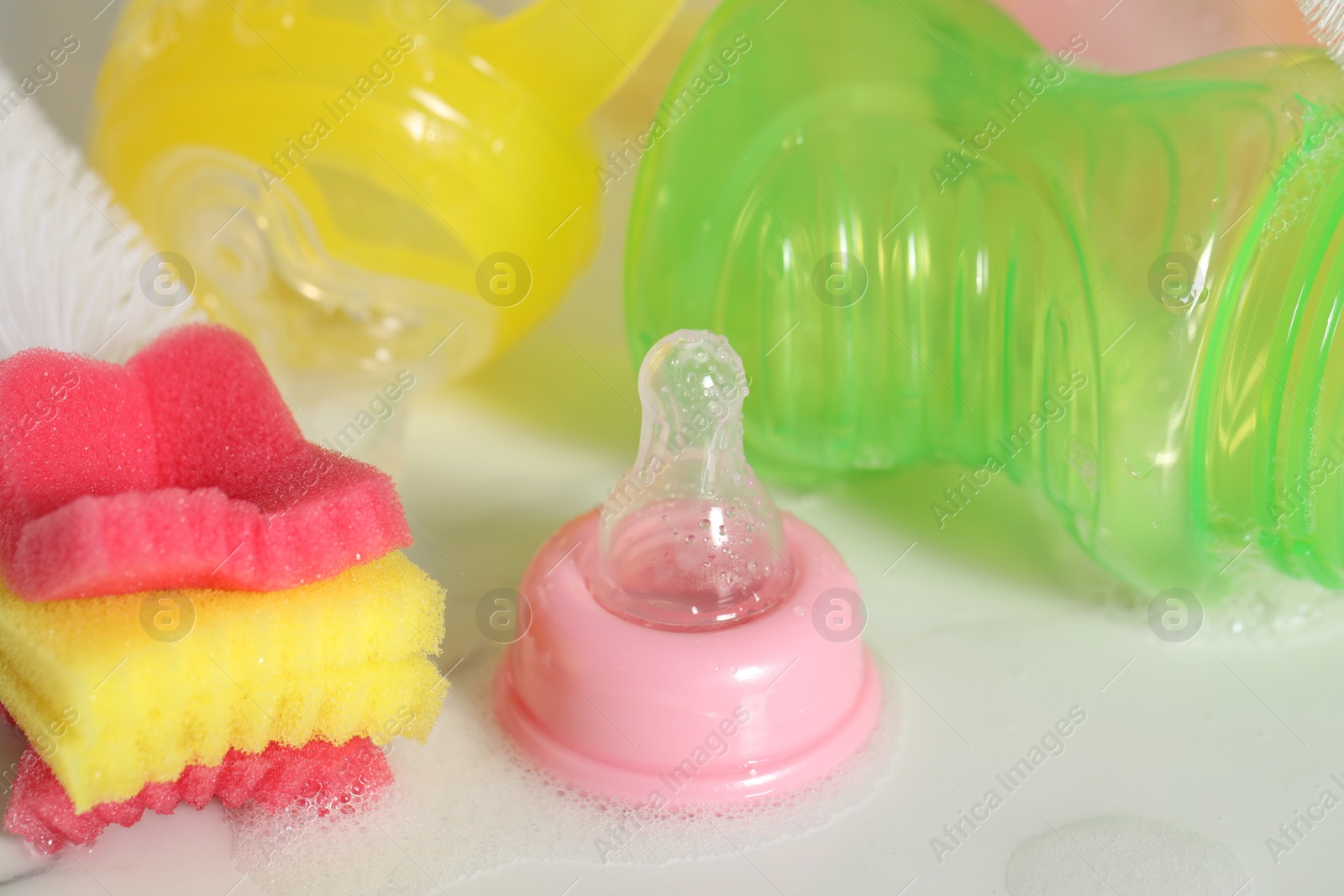 Photo of Wet baby bottles and nipple after sterilization near sponge on white table, closeup