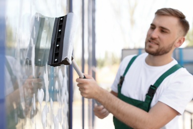 Photo of Male cleaner wiping window glass with squeegee from outside