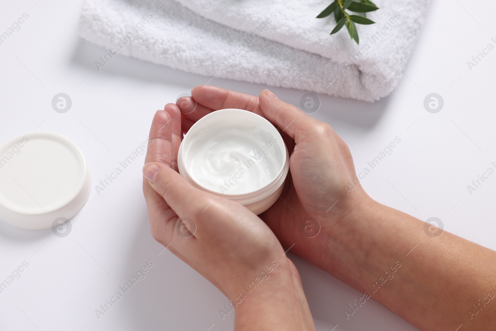 Photo of Woman with jar of hand cream, towel and green leaves on white background, closeup