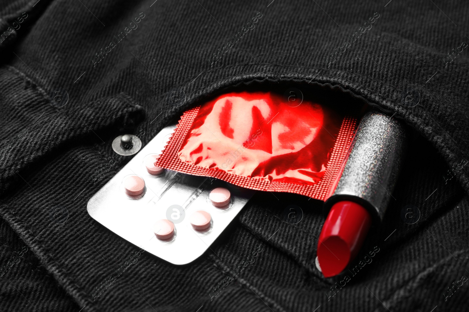 Photo of Red lipstick with condom and birth control pills in pocket of jeans, closeup. Safe sex concept