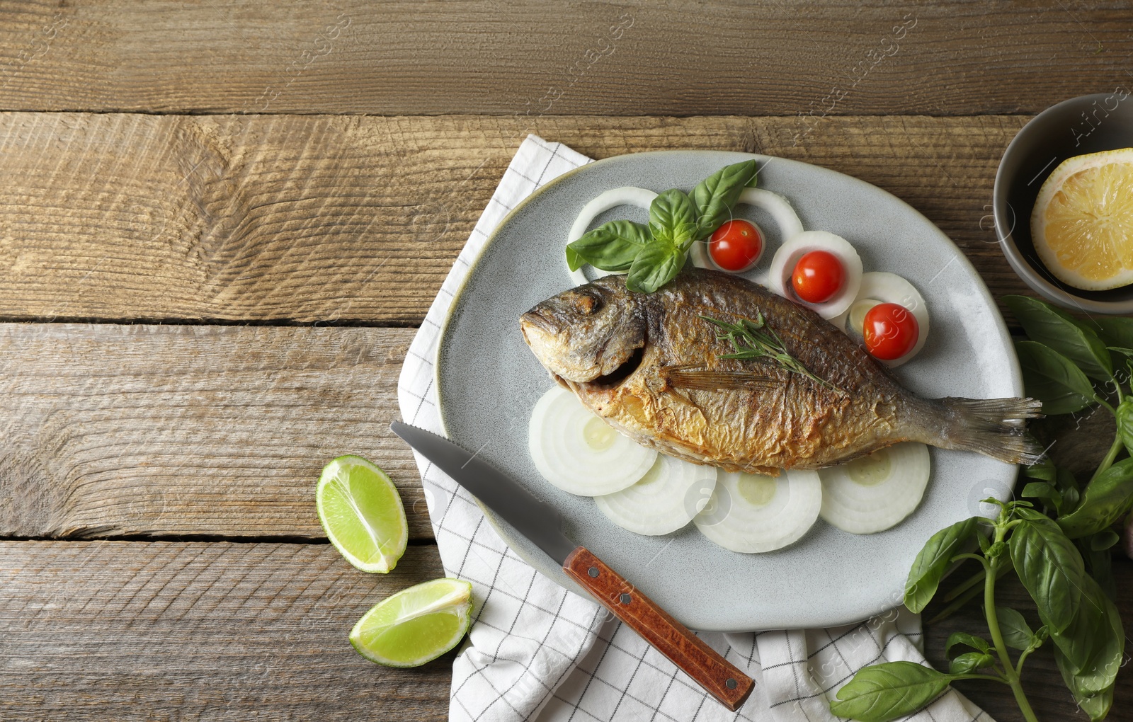 Photo of Delicious dorado fish with vegetables and herbs served on wooden table, flat lay. Space for text