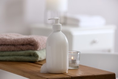 Photo of Bottle of bubble bath with foam, towels and candle on tub in bathroom