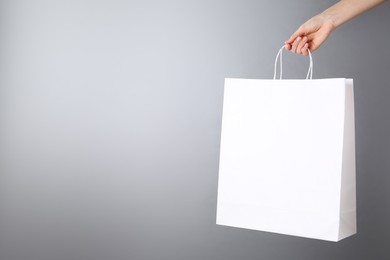 Photo of Woman holding white paper bag on grey background, closeup with space for text. Mockup for design