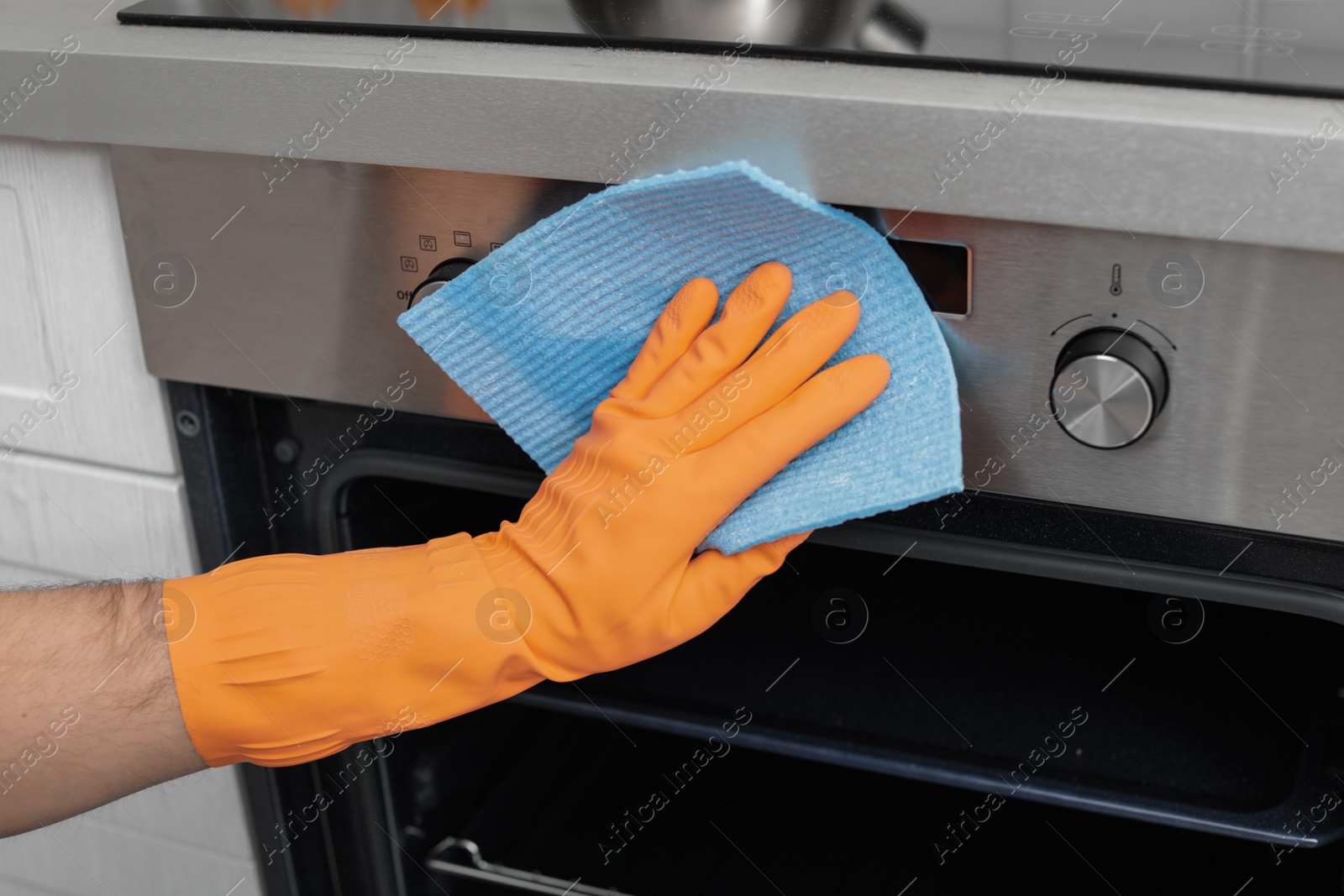 Photo of Young man cleaning oven with rag in kitchen, closeup