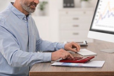 Professional accountant using calculator at wooden desk in office, closeup