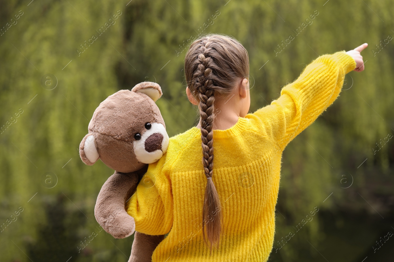 Photo of Little girl with teddy bear outdoors, back view