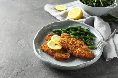 Tasty schnitzels served with lemon and green beans on grey table, closeup