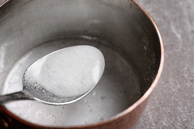 Photo of Chemical reaction of vinegar and baking soda in spoon over saucepan on table