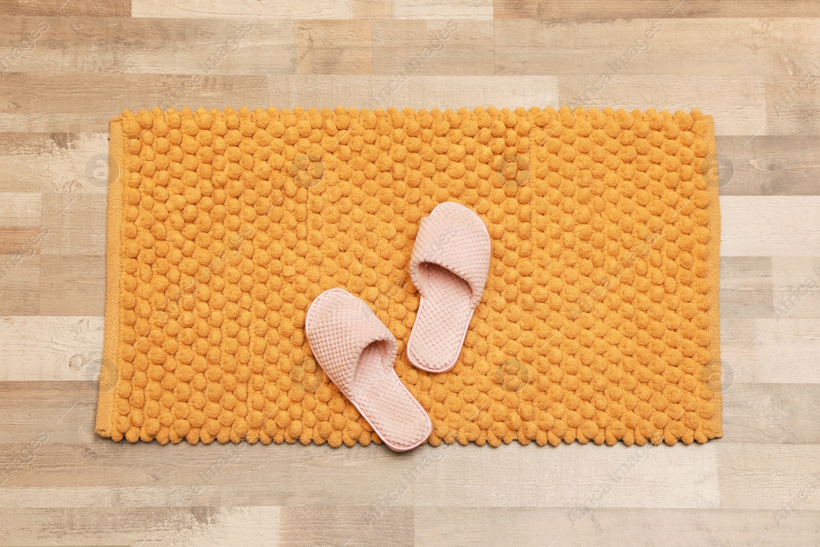 Photo of New yellow bath mat with soft slippers on floor, top view