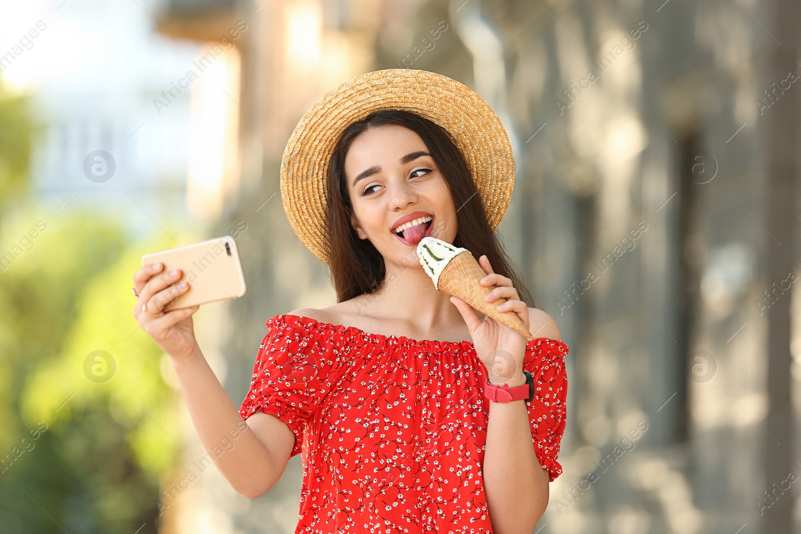 Photo of Happy young woman with delicious ice cream in waffle cone taking selfie outdoors