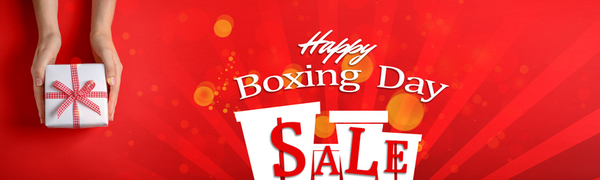 Boxing day sale banner design. Woman holding gift on red background, closeup