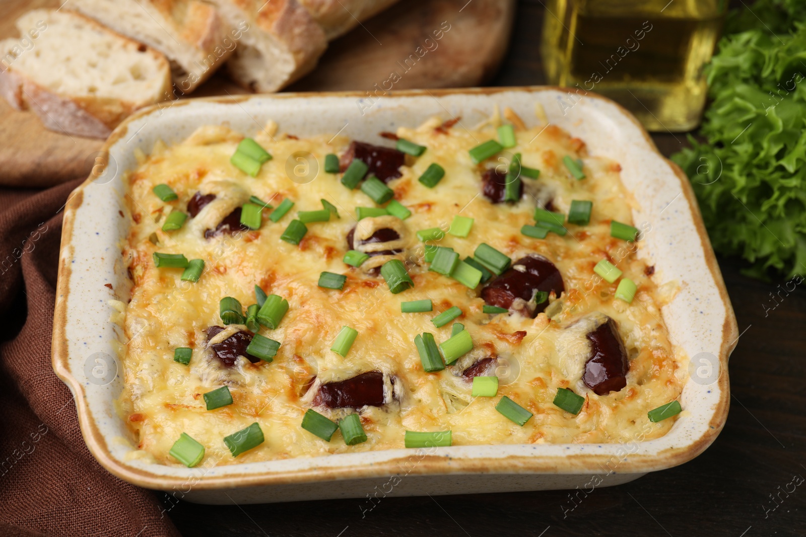 Photo of Tasty sausage casserole with green onions in baking dish on wooden table, closeup