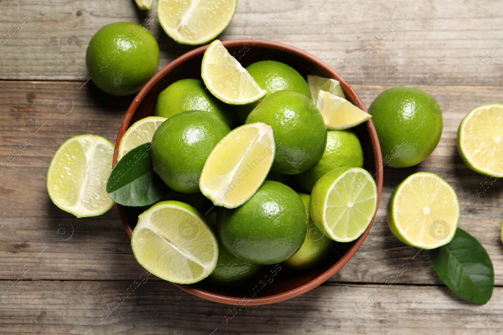 Photo of Tasty ripe limes in bowl on wooden table, top view