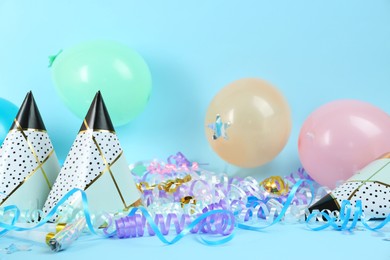 Photo of Colorful serpentine streamers, caps, party horns and balloons on light blue background