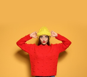 Young woman in warm sweater and knitted hat on color background. Celebrating Christmas