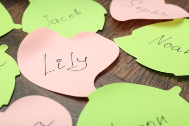 Paper stickers with different names on wooden table, closeup. Choosing baby's name