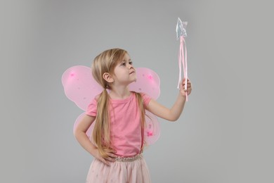 Photo of Cute little girl in fairy costume with pink wings and magic wand on light grey background