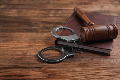 Photo of Gavel, handcuffs and book on wooden table, space for text. Criminal law