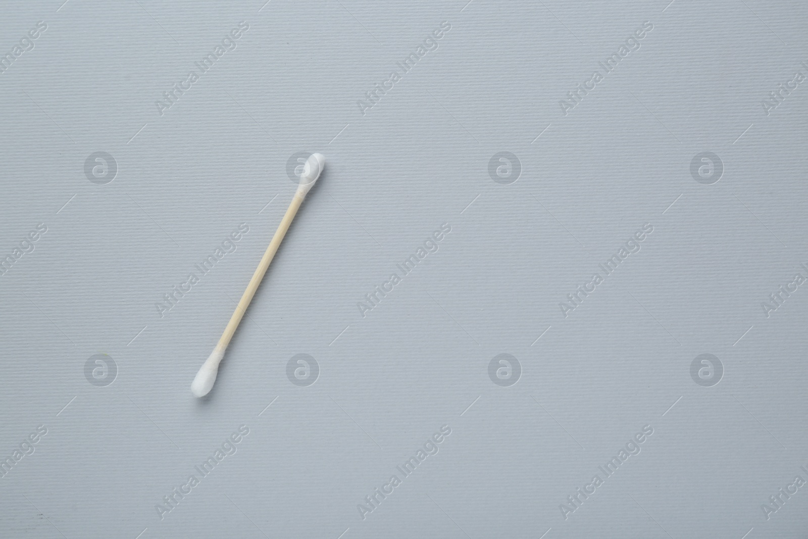 Photo of One wooden cotton bud on light grey background, top view. Space for text