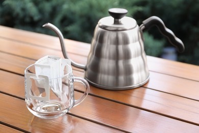 Photo of Glass cup with drip coffee bag and kettle on wooden table