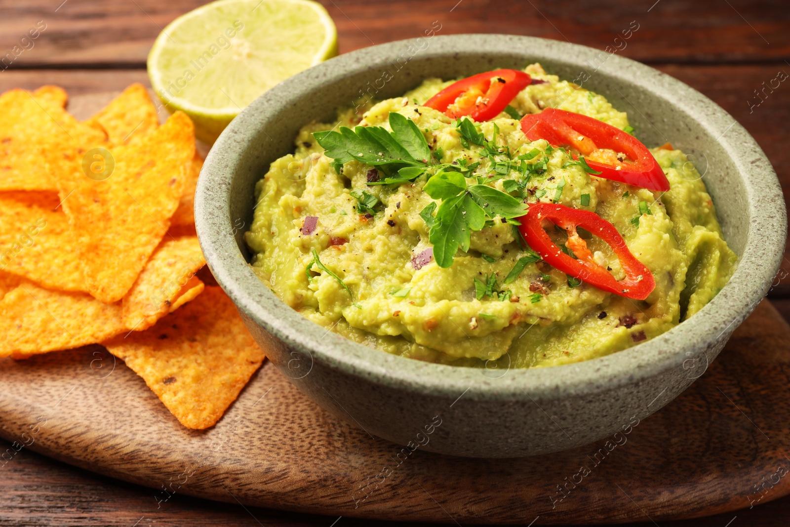 Photo of Bowl of delicious guacamole, lime and tortilla chips on wooden table, closeup