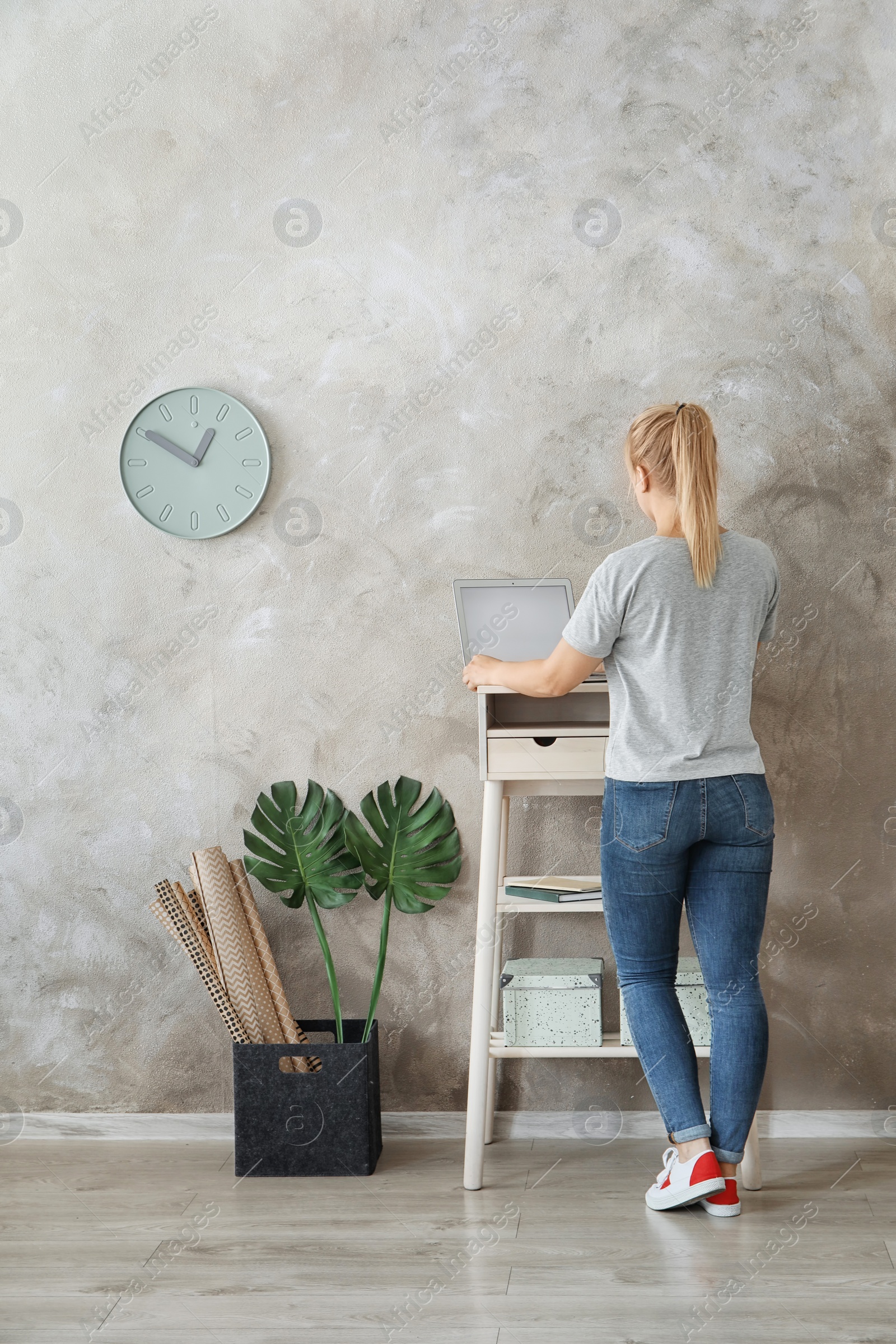 Photo of Young woman using laptop at stand up workplace in room