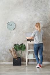 Photo of Young woman using laptop at stand up workplace in room