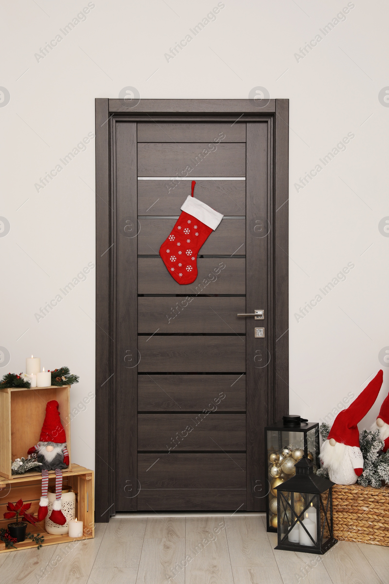 Photo of Christmas stocking hanging on wooden door and festive decoration indoors