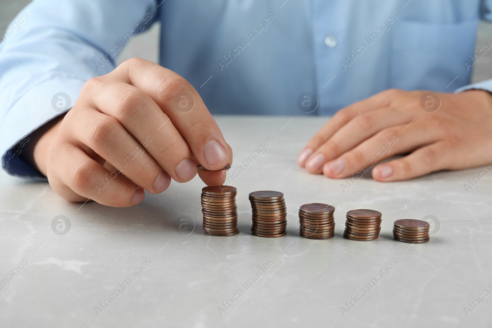 Photo of Man stacking coins on grey stone table, closeup view