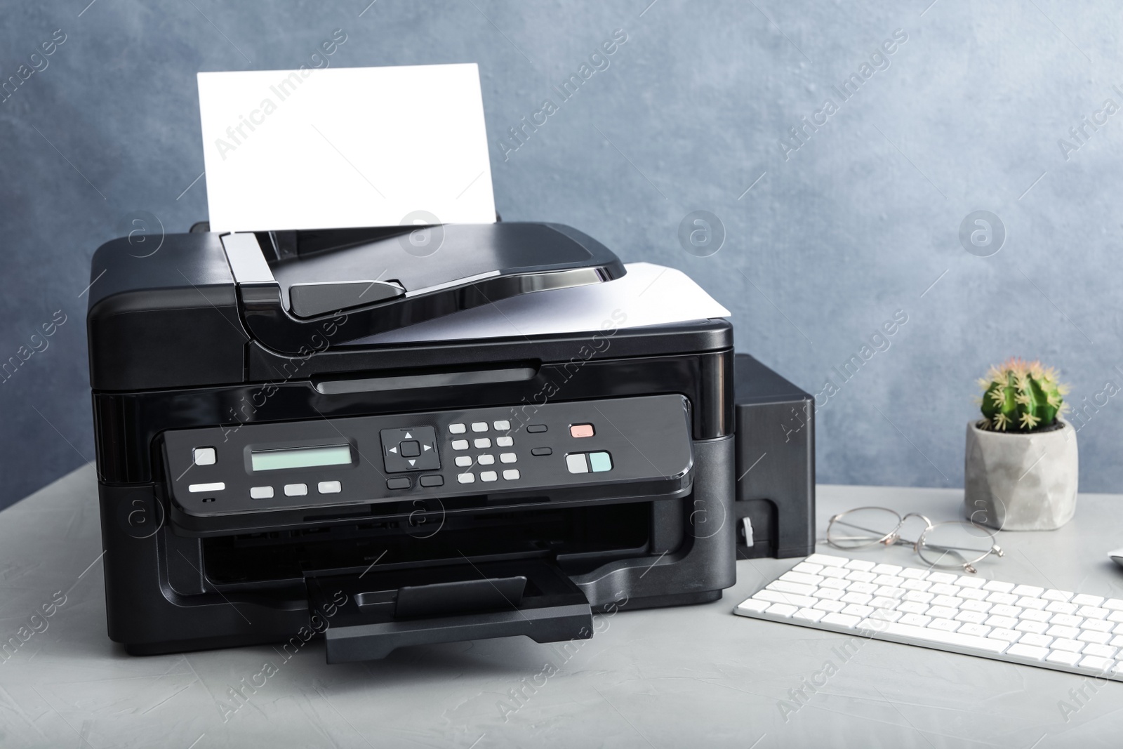 Photo of Modern printer with paper and computer keyboard on grey table