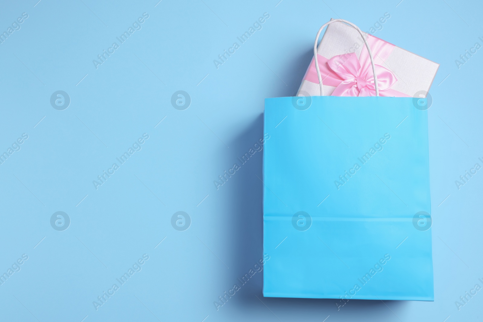 Photo of Bright paper shopping bag with gift box on light blue background, top view. Space for text