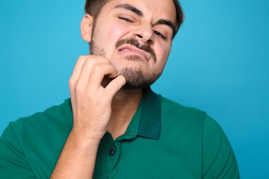 Young man scratching face on color background. Annoying itch