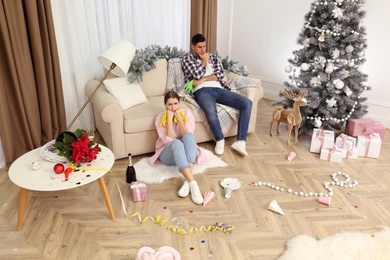 Photo of Tired couple sitting in messy room while cleaning after New Year party