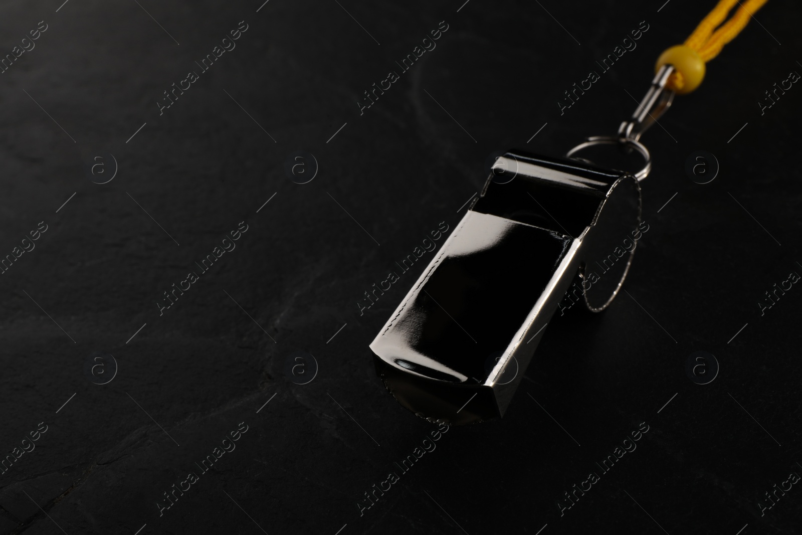 Photo of Referee equipment. Metal whistle on black textured background, closeup and space for text