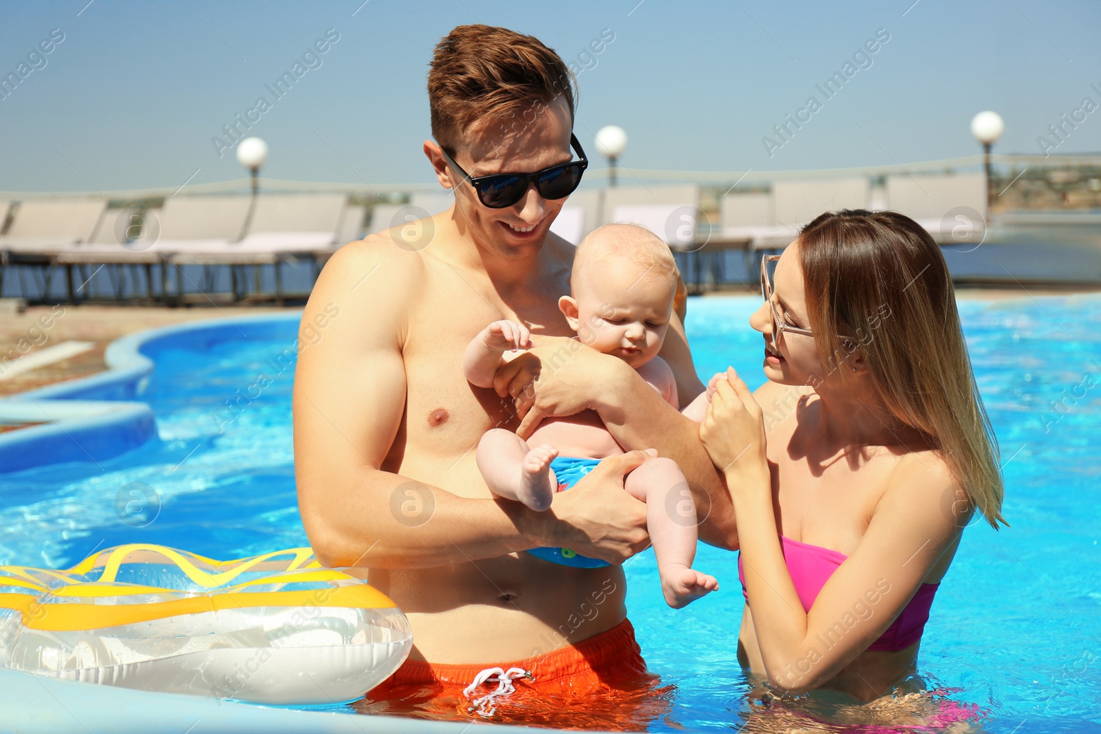 Photo of Happy parents with little baby in swimming pool on sunny day